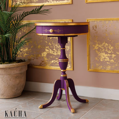 Purple side table with gold accents in a room with decorative wall art and a plant.