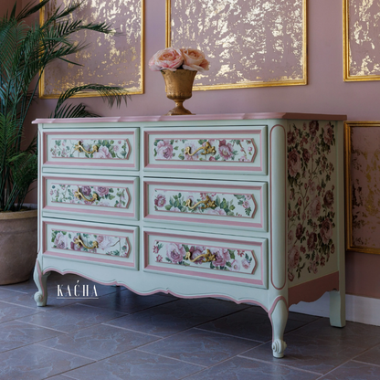 Decorative chest of drawers with floral patterns in a room with pink walls and framed artwork.